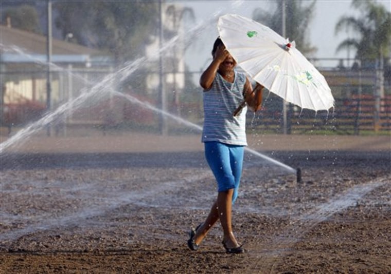A girl plays in the sprinklers to beat the heat in Monterey Park, Calif. on Monday. Southern California Edison says more than 27,000 of its customers were without power Tuesday morning, mainly in Orange and Los Angeles counties. 